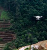 Cinematic drone capturing a traveler standing on a cliff at golden hour overlooking mountains and ocean, representing aerial storytelling and filmmaking